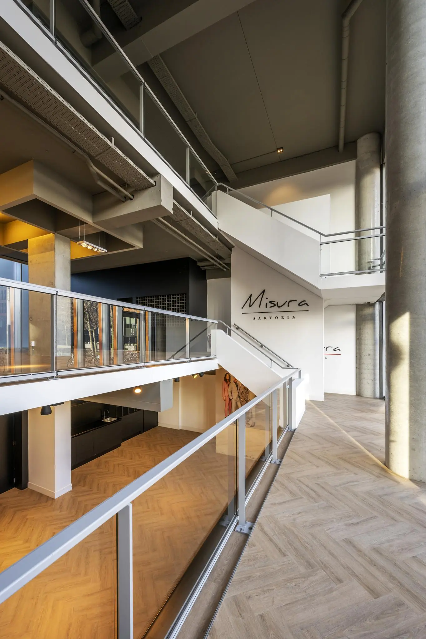 Moderne, open interieur met glazen balustrades en houten visgraatvloer in het Misura-gebouw aan het George Gershwinplein.